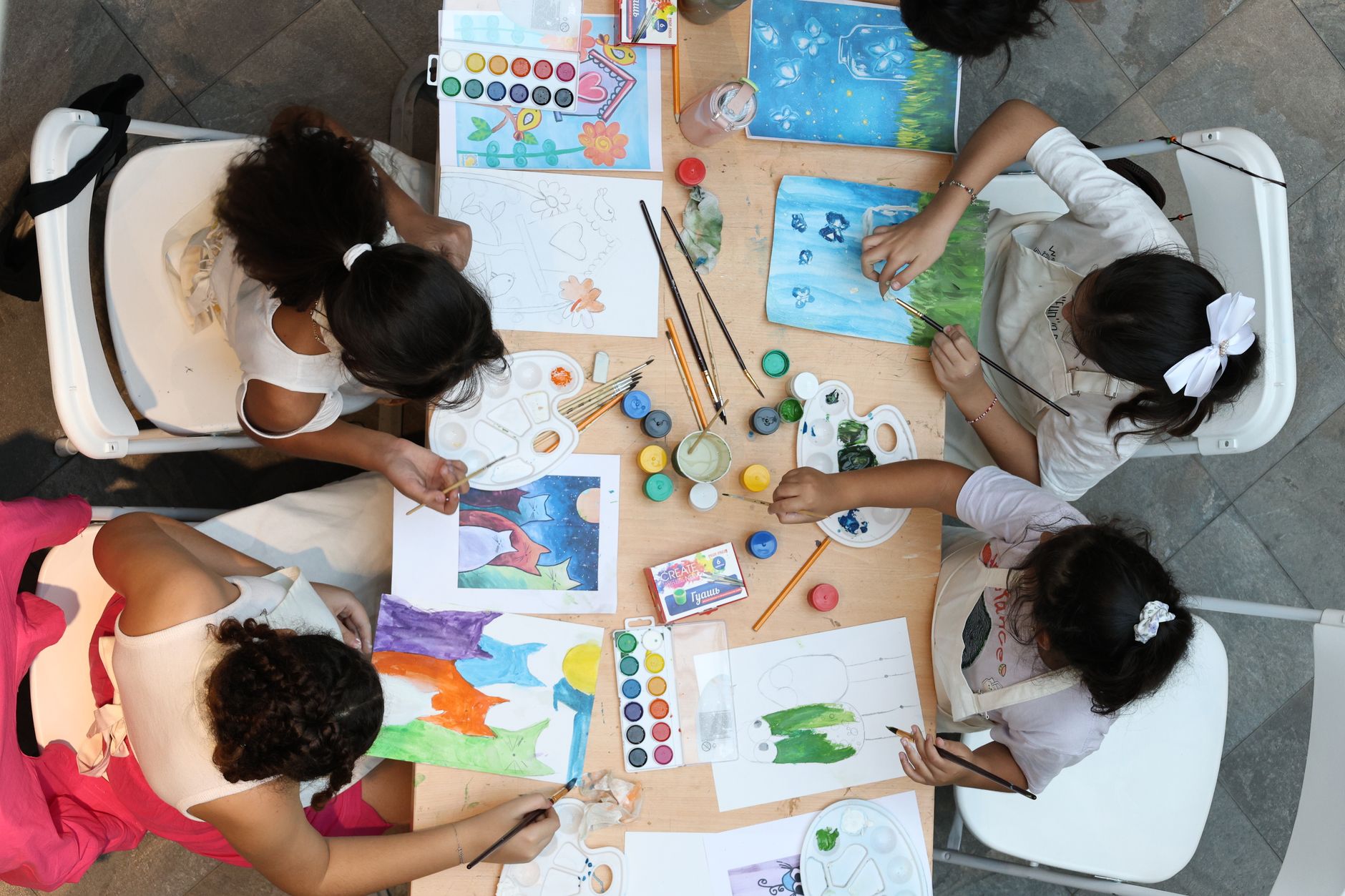 Djeca za stolom crtaju i slikaju vodenim bojama